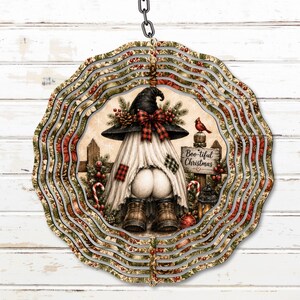 May include: A circular metal wind spinner featuring a gnome wearing a black hat with a red plaid bow, white fabric, and brown boots. The design includes holly, pine branches, a red cardinal, and a wooden sign that reads Boo-tiful Christmas.