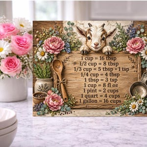 Op de afbeelding: Een rechthoekig houten bord met een illustratie van een geitje, bloemaccenten en een tabel voor keukenmaten. De tekst luidt: 1 cup = 16 tbsp, 1/2 cup = 8 tbsp, 1/3 cup = 5 tbsp + 1 tsp, 1/4 cup = 4 tbsp, 1 tbsp = 3 tsp, 1 cup = 8 fl oz, 1 pint = 2 cups, 1 quart = 4 cups, 1 gallon = 16 cups.