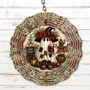 May include: A circular metal wind spinner featuring a ghost wearing a witch hat, boots, and a plaid-patched sheet. The ghost holds a red mug with a heart, standing near a sign that reads Merry Christmas, a lantern, and a snowy house.