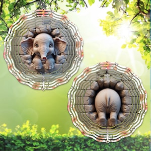 May include: Two decorative elephant wind spinners. One shows the elephant's face, the other its rear. Each has a layered, circular design with a floral pattern around the edge. The elephant is gray, and the background is green.