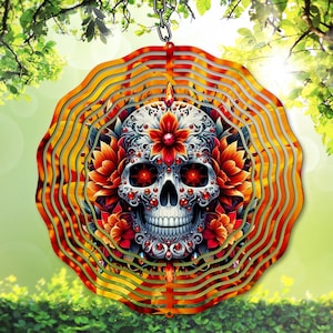 Könnte beinhalten: Ein dekorativer Metall-Windspinner mit einem detaillierten Totenkopf-Design und floralen Akzenten. Der Totenkopf ist mit roten Edelsteinen verziert und von orangefarbenen und roten Blumen umgeben. Der Windspinner hängt an einer Kette.