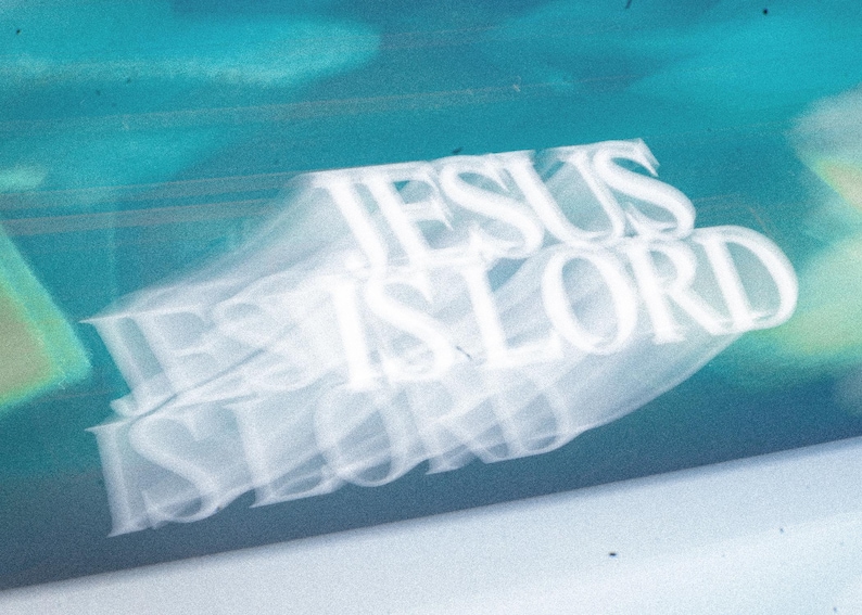 May include: An abstract image with the words "JESUS IS LORD" in white, layered over a blurred, teal and blue background. The text appears to be slightly transparent, creating a ghostly effect.