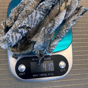 May include: A digital kitchen scale with a blue platform displays 4.10 ounces. Dried fish is on the scale.