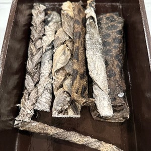 May include: A collection of six different dog chews made from dried animal parts. The chews are in a brown wooden box.