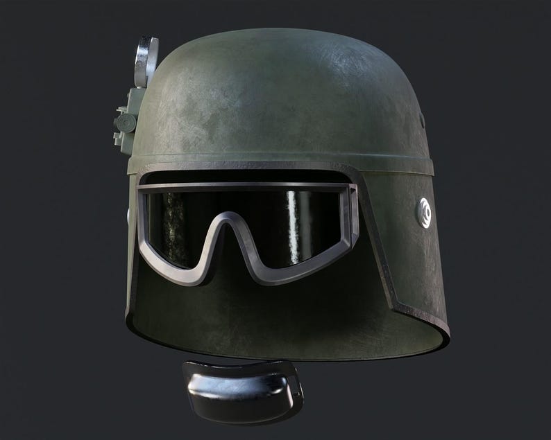 May include: An olive drab helmet with a visor and a silver-colored attachment on top. The helmet has a curved visor with a silver frame. A dark, curved piece is below the helmet.