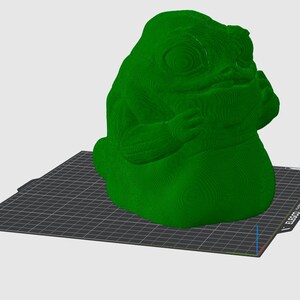 Puede incluir: Una figura verde impresa en 3D de una criatura grande con forma de babosa y superficie texturizada. La figura est&aacute; sobre una superficie negra con patr&oacute;n de cuadr&iacute;cula. La figura tiene un dise&ntilde;o org&aacute;nico detallado.