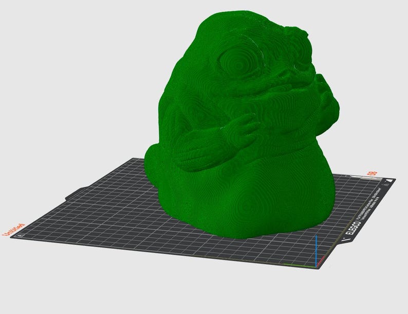 Puede incluir: Una figura verde impresa en 3D de una criatura grande con forma de babosa y superficie texturizada. La figura est&aacute; sobre una superficie negra con patr&oacute;n de cuadr&iacute;cula. La figura tiene un dise&ntilde;o org&aacute;nico detallado.