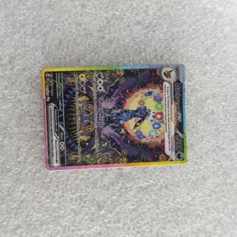 May include: A rectangular Umbreon ex trading card featuring a dark, stylized illustration of the creature surrounded by a vibrant, circular pattern of colorful gems. The card displays the text Moon Mirage, Onyx, and 280 HP with a holographic finish.