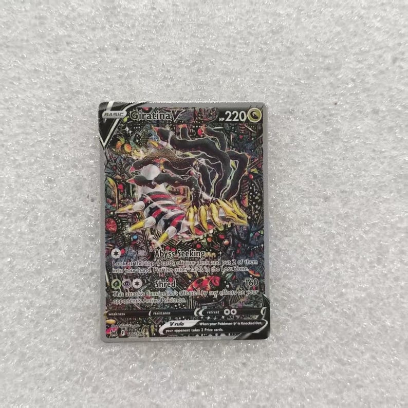May include: A Giratina V trading card with 220 HP, featuring a dark, intricate illustration of the legendary creature with multiple appendages. The card displays the text Abyss Seeking and Shred, along with game mechanics and a black and silver border.