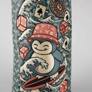 May include: A cylindrical golf club head cover featuring a dark green chevron pattern background. The design depicts a cartoon creature wearing a red bucket hat, surfing on a wave, surrounded by red dice, playing cards, and a roulette wheel.