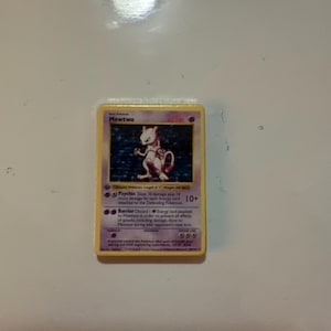 May include: A Mewtwo trading card with a yellow border and purple text box. The card features a holographic illustration of the character Mewtwo, with the name Mewtwo printed at the top, 60 HP, and text describing Psychic and Barrier attacks.