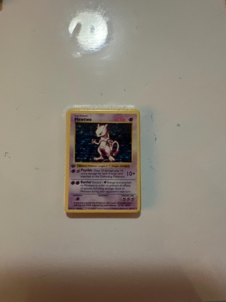 May include: A Mewtwo trading card with a yellow border and purple text box. The card features a holographic illustration of the character Mewtwo, with the name Mewtwo printed at the top, 60 HP, and text describing Psychic and Barrier attacks.