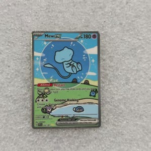 May include: A Mew ex trading card featuring a light blue Mew character centered in a blue circle against a sky background. The card displays 180 HP, the Ability Restart, and the Genome Hacking attack, with green grassy terrain and small illustrations of other creatures.
