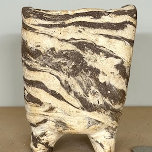 May include: A small, hand-built ceramic planter with a marbled, swirled pattern of dark brown and off-white clay. The vessel features a rectangular, slightly tapered body supported by four short, sturdy feet, with a visible US quarter coin for scale.