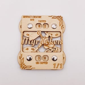 May include: A wooden Myr Token with the text "Myr Token" and the words "Artifact Creature" and "Tapped" and "Un-Tapped". The token has silver rivets and the numbers 8, 2, 3, 9, and 1/1.