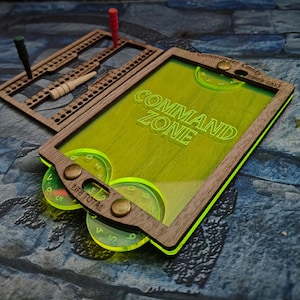 May include: A wooden game board with a green acrylic insert that reads "COMMAND ZONE". The board has a life total tracker and a dice rolling area. The board is made of wood and has a green and brown colour scheme.