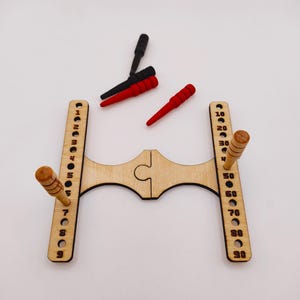 May include: A wooden cribbage board with two wooden pegs and three coloured pegs. The board has two vertical columns with numbers and two wooden pegs. The pegs are red, black, and red.