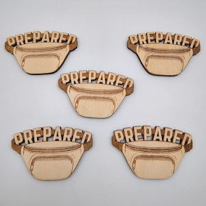 Puede incluir: Cinco recortes de riñoneras de madera con la palabra "PREPARED" encima de cada bolsa. Las riñoneras son de color marrón claro con un contorno y detalles de cremallera en marrón más oscuro. El texto también es marrón oscuro.