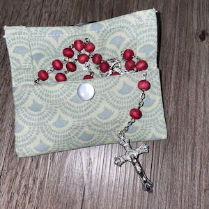 May include: A red wooden rosary with a silver crucifix, stored in a light green fabric pouch with a white button.