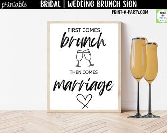 May include: A rectangular sign in a light wood frame featuring black text on a white background that reads: FIRST COMES brunch, THEN COMES marriage. The design includes a line drawing of two clinking champagne flutes and a heart symbol below the text.