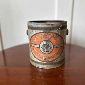 May include: Vintage Cottolene tin with an orange and white label. The label features the text "Cottolene" and "N.K. Fairbank Company". The tin has a silver finish and small handles on each side.