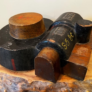 May include: A vintage wooden hat block with a black painted surface and a round top. The block is marked with the number "35 82" and the number "333".