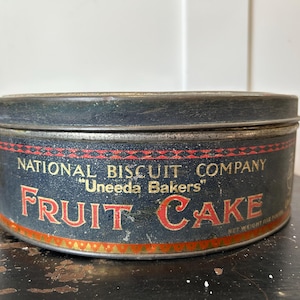 May include: Vintage National Biscuit Company "Uneeda Bakers" fruit cake tin. The round tin is dark blue with red and gold lettering. The words "Fruit Cake" are prominently displayed in a bold, red font.