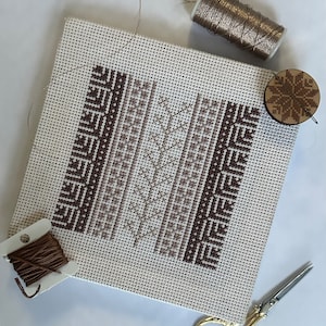 Pode incluir: Uma tela branca com um padrão geométrico marrom e bege costurado sobre ela. Há um carretel de fio dourado metálico, um carretel de fio marrom, um par de tesouras douradas e um ornamento de madeira em forma de floco de neve.