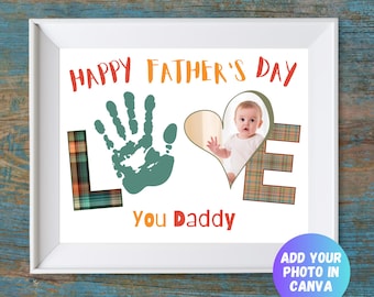 Puede incluir: Una impresión enmarcada con el texto HAPPY FATHER'S DAY en la parte superior y YOU DADDY en la inferior. La palabra LOVE se forma con una L de cuadros, una huella de mano verde como O, una foto de bebé en forma de corazón como V y una E de cuadros.
