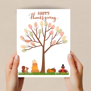 Op de afbeelding: Een witte kaart met de tekst "Happy Thanksgiving" in bruin cursief schrift. In het midden van de kaart staat een bruine boom met groene, oranje en gele bladeren. Onderaan de kaart staan drie pompoenen, een eekhoorn en een kalkoen met een pelgrimhoed.