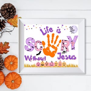 May include: A white framed print featuring the text Life is Scary Without Jesus in purple and pink lettering. The letter A is replaced by an orange handprint. The design includes a full moon with bats, a spider, and a row of small pumpkins.