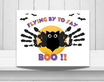Puede incluir: Una impresión rectangular con una luna amarilla central y una silueta de búho hecha con huellas de manos negras. El texto dice FLYING BY TO SAY BOO!! en morado y naranja. Pequeños murciélagos negros están dispersos sobre un fondo blanco.