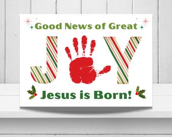 May include: A rectangular sign featuring the text Good News of Great Joy and Jesus is Born in green. The word JOY is written with the letter O replaced by a red handprint, while the letters J and Y feature a red, white, and green candy cane pattern.