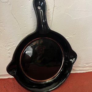 May include: Black cast iron skillet with a gold rim. The skillet has a handle and is a decorative wall hanging.
