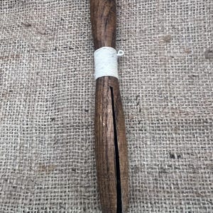 May include: A vintage wooden clothes pin with a dark brown finish. The clothes pin is wrapped with white twine. The clothes pin is approximately 8 inches long.