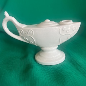 May include: White ceramic genie lamp with a decorative design. The lamp has a round base and a spout on the top.