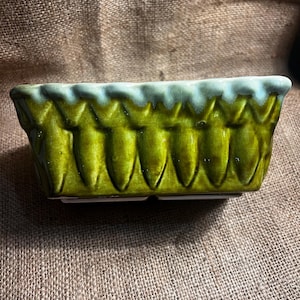 May include: A green and white ceramic planter with a scalloped rim and a textured design. The planter is rectangular and has a slightly rounded bottom.