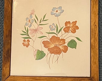 May include: A framed ceramic tile with a floral design. The tile features a bouquet of flowers in shades of pink, blue, and orange, painted on a white background.