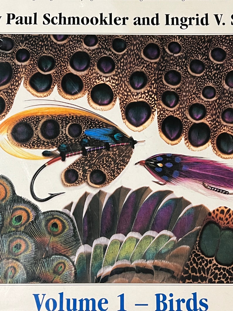 May include: A book cover featuring a variety of colorful bird feathers, including peacock, pheasant, and other exotic species. The title "Volume 1 - Birds" is printed in blue on a white background.