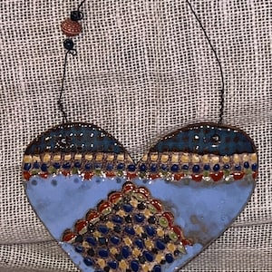 May include: A blue ceramic heart with a multi-colored geometric pattern. The heart has a string attached to the top with a brown and black bead.