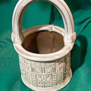 May include: White ceramic planter with a handle, featuring an embossed geometric design. The planter has a brown interior.