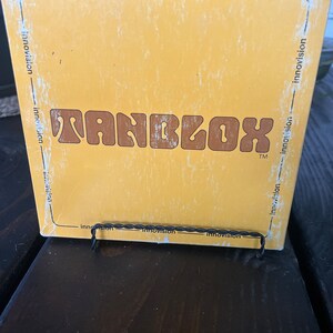 May include: A yellow box with the word "TANBLOX" in brown letters. The box has the word "innovation" printed on all sides.
