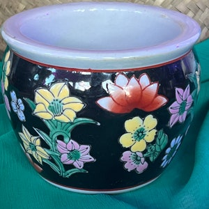 May include: A black ceramic planter with a white rim and floral designs in shades of yellow, red, pink, and green. The flowers are stylized and have a traditional Asian aesthetic.