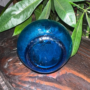 Puede incluir: Un jarr&oacute;n de vidrio azul oscuro con una abertura redonda y ancha. El jarr&oacute;n est&aacute; sobre una superficie de madera.
