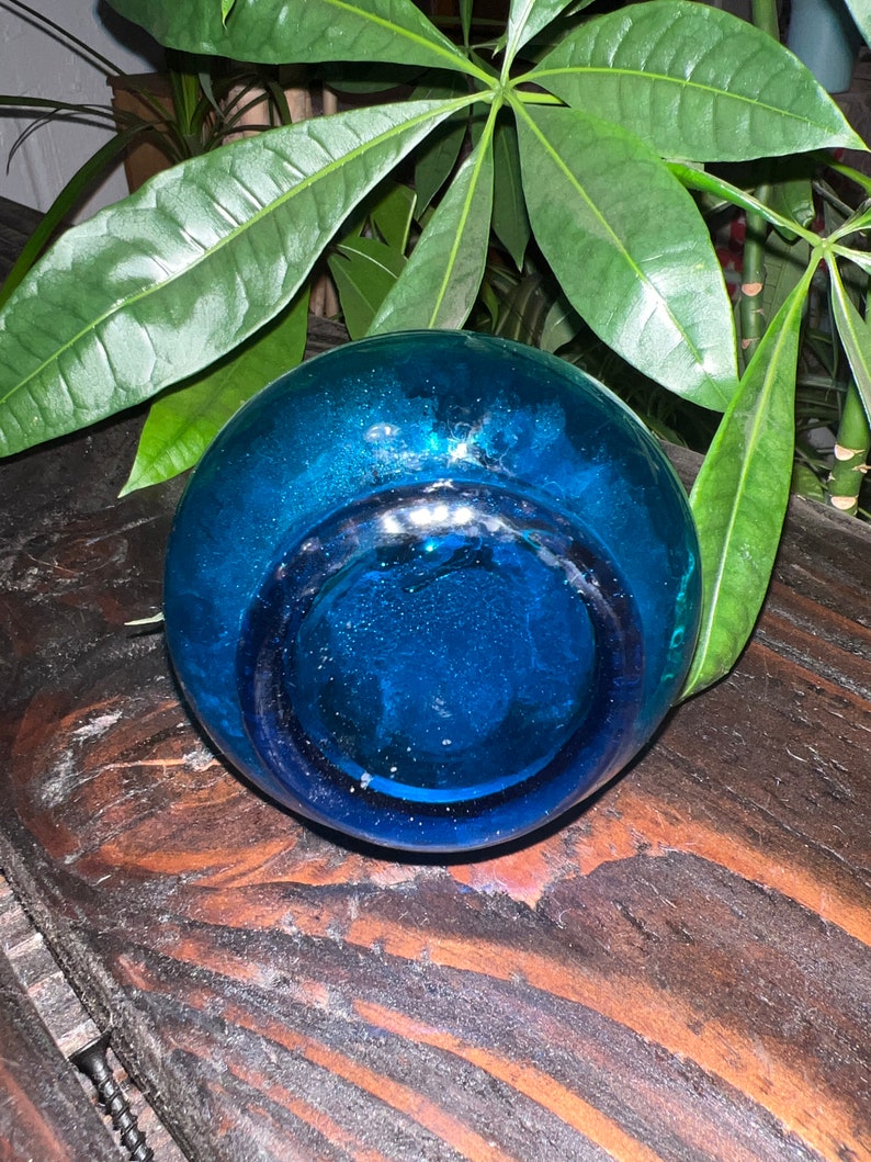 Puede incluir: Un jarr&oacute;n de vidrio azul oscuro con una abertura redonda y ancha. El jarr&oacute;n est&aacute; sobre una superficie de madera.