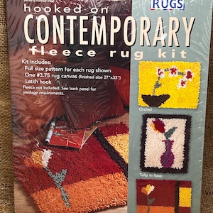 May include: A Leisure Arts Hooked on Contemporary fleece rug kit in plastic packaging. The kit includes a full size pattern, a #3.75 rug canvas with a finished size of 27 inches by 33 inches, and a latch hook. The packaging displays three floral rug designs.