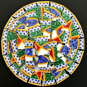 May include: A circular mosaic arrangement composed of numerous ceramic shards. Each piece features a repeating pattern of white zigzag lines on a blue band, alongside sections of textured green, mottled blue, and solid red with yellow borders.