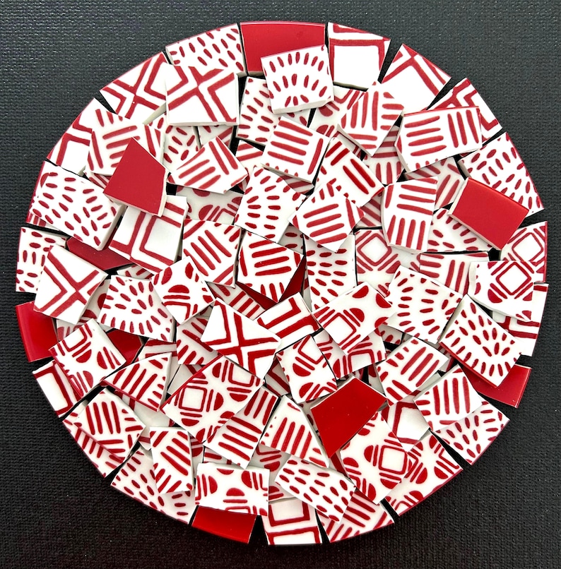 May include: A circular collection of ceramic mosaic tiles arranged in a dense pattern. The tiles are primarily white with red geometric designs, including stripes, dashes, and solid red shapes, creating a cohesive, multi-piece decorative surface.