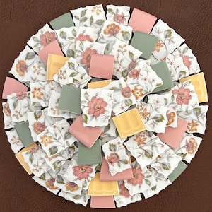 May include: Circular mosaic design composed of floral patterned porcelain shards and square tiles in shades of pink, yellow, and green. The mosaic is arranged on a brown surface, creating a decorative and artistic display.