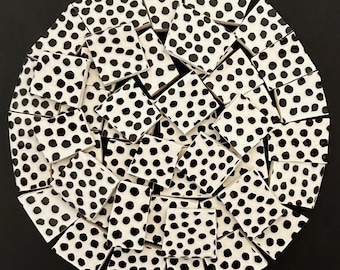 May include: A circular arrangement of white ceramic tiles with black polka dots. The tiles are arranged in a mosaic pattern, creating a visually interesting design. The background is solid black.